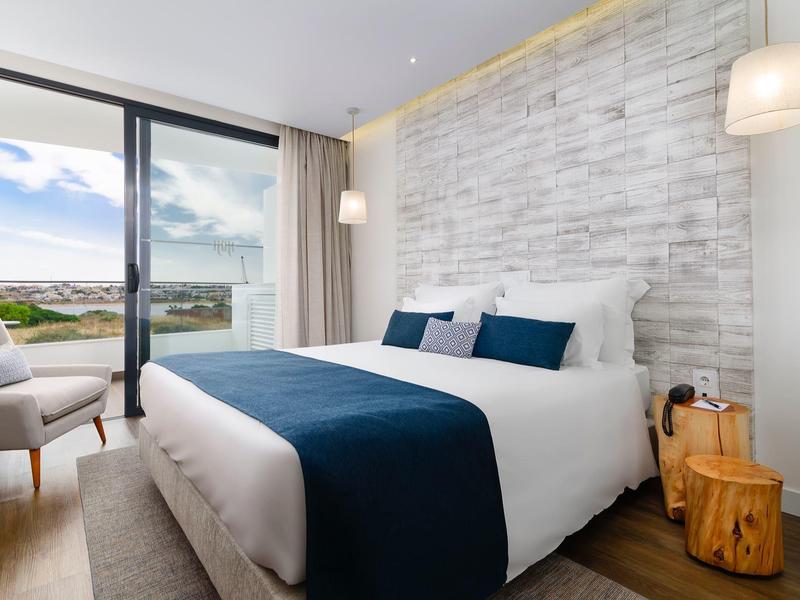Moderní hotelový pokoj s manželskou postelí, výhledem na moře a jednoduchým zařízením.