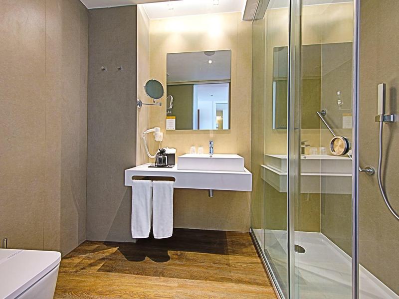 Moderní koupelna se skleněnou sprchou, zavěšeným umyvadlem a toaletou.