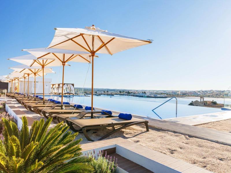 Slunná oblast bazénu s lehátky a bílými slunečníky u moře.