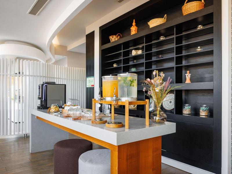 Nápojová stanice s dávkovači džusů a občerstvením před černými regály v moderní hotelové části