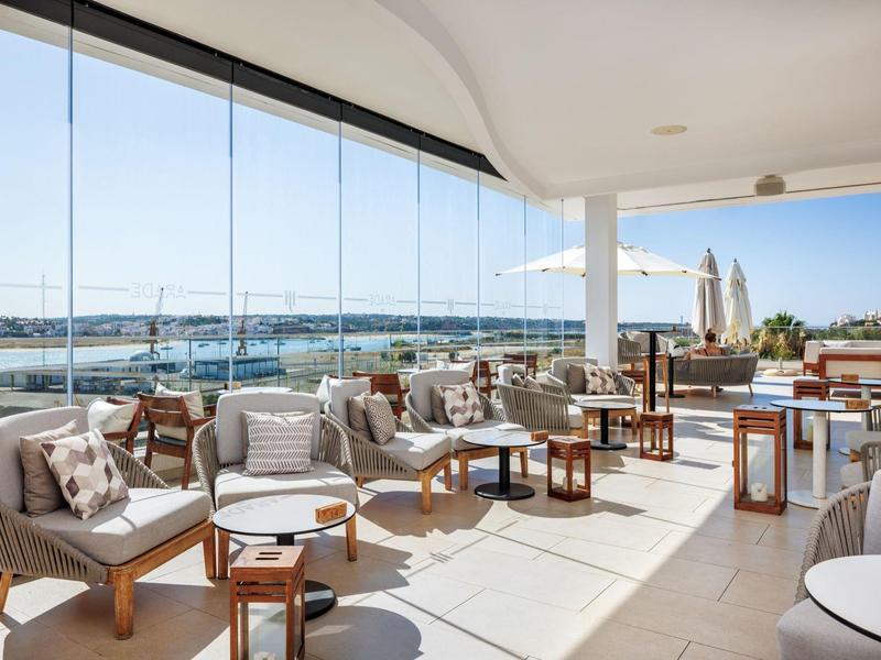 Terasa s pohodlnými pohovkami a stoly s výhledem na přístav za jasné oblohy.