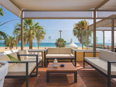 Coin salon moderne sur une terrasse avec vue sur des palmiers et la mer par ciel clair.