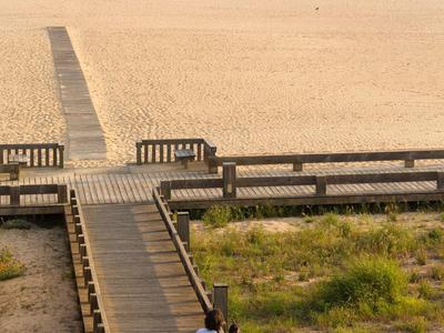 Un couple en vêtements blancs sur une passerelle en bois surplombant la plage et la mer.