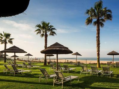 Pelouse verte avec palmiers et parasols au bord de la mer sous un ciel dégagé.