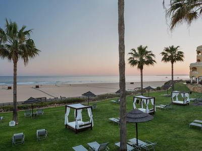 Coucher de soleil à la plage avec des palmiers, des transats et des petites cabanes sur une pelouse verte.
