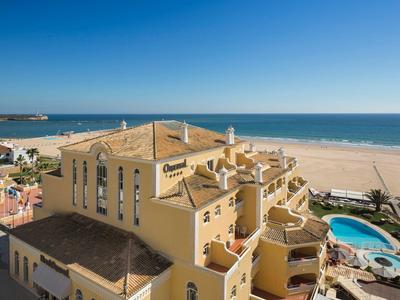 Bâtiment d'hôtel jaune avec panneaux solaires et piscine à côté d'une plage de sable au bord de la mer.