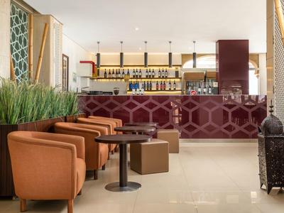 Espace bar d'hôtel moderne avec fauteuils bruns et comptoir rouge foncé.