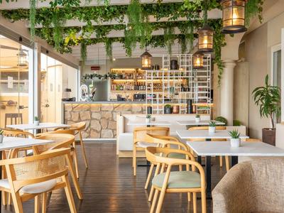 Restaurant d'hôtel moderne avec des chaises en bois, des tables blanches et des plantes vertes suspendues au plafond.