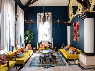 Espace lounge élégant d'hôtel avec canapés jaunes, poutres en bois et lustre.