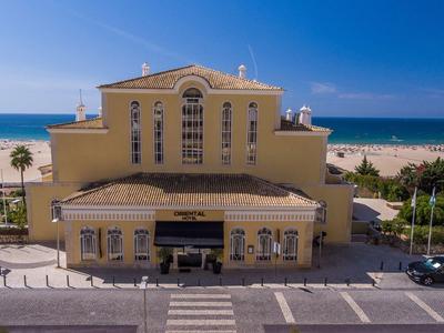 Grand bâtiment jaune près de la plage avec la mer en arrière-plan et un parking devant.