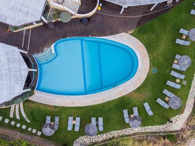 Piscine ovale avec eau bleue entourée de chaises longues sur pelouse verte près d'une terrasse en bois.