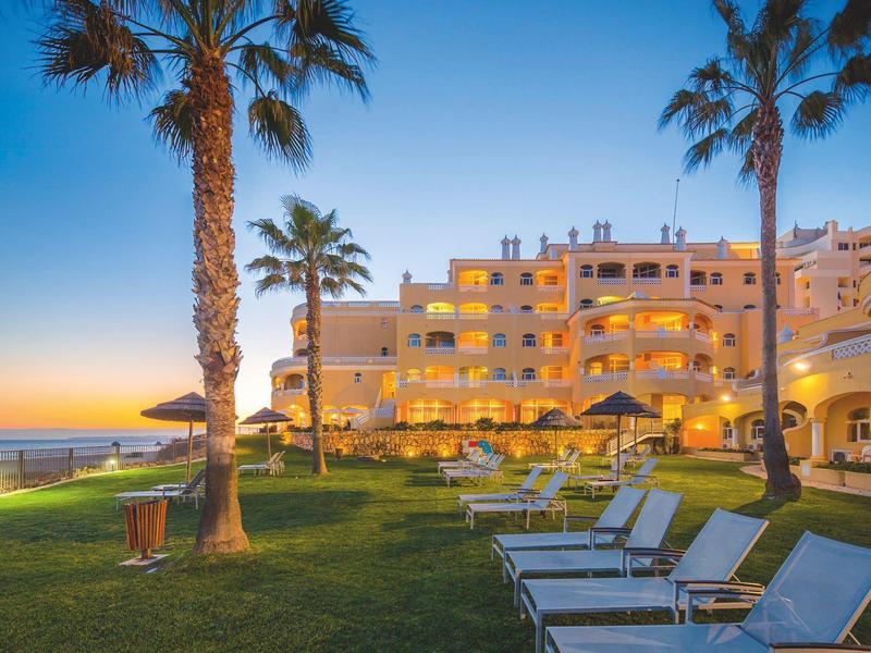 Complexe hôtelier avec chaises longues et palmiers sur une plage ensoleillée au coucher du soleil.