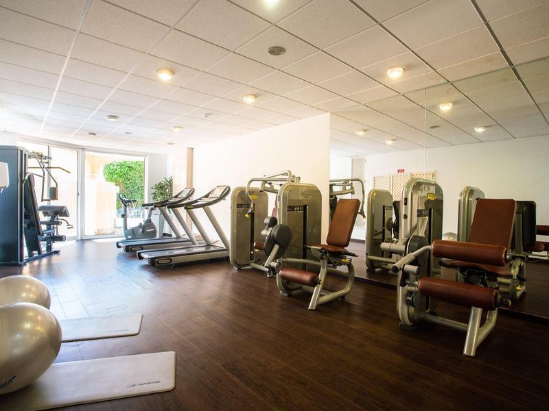 Salle de sport moderne avec appareils et tapis roulants dans une pièce lumineuse au sol en bois.