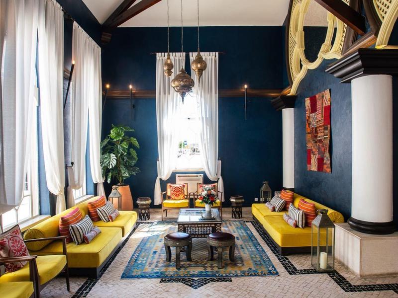 Espace lounge élégant d'hôtel avec canapés jaunes, poutres en bois et lustre.