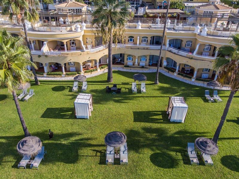 Vue d'un hôtel à plusieurs étages avec des chaises longues et une pelouse verte avec des palmiers