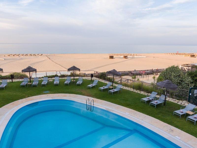 Vue d'une piscine avec transats et plage en arrière-plan sous un ciel nuageux