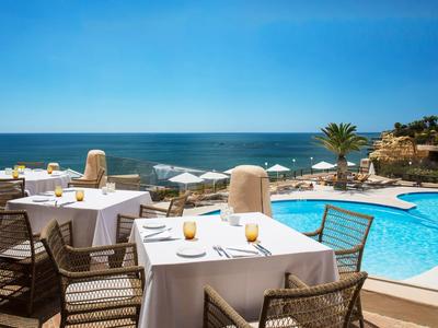 Terrasse d'hôtel avec tables dressées, piscine et vue sur la mer sous un ciel clair.