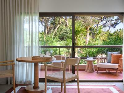 Chambre lumineuse avec mobilier en bois et vue sur une terrasse verte avec des sièges.