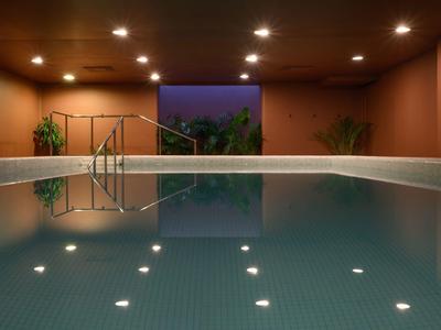 Piscine intérieure éclairée avec plantes dans un espace spa moderne le soir.