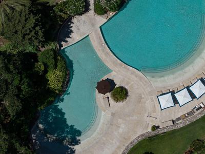 Vue aérienne de deux piscines avec chaises longues et espace jardin vert à côté.