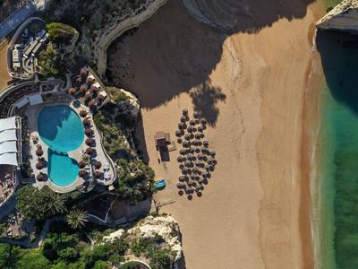 Vue aérienne d'un hôtel avec piscine, plage de sable et chaises longues près de l'eau claire.