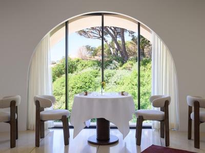 Une table élégamment dressée pour deux devant une grande fenêtre voûtée donnant sur des arbres verts.