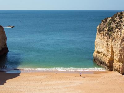 Plage de sable vide entre de hautes falaises avec une mer bleue calme en arrière-plan.