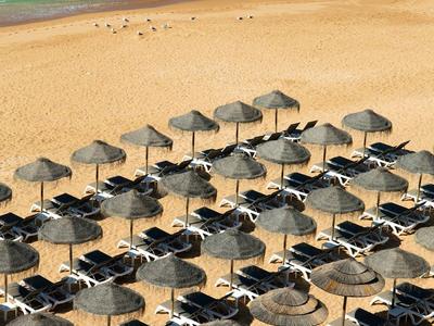 Rangées de parasols et de chaises longues sur une plage de sable avec la mer bleue en arrière-plan.