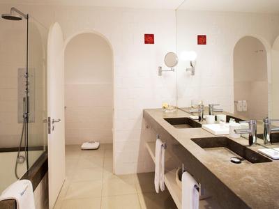 Salle de bain moderne avec carrelage beige, double vasque et paroi de douche en verre.