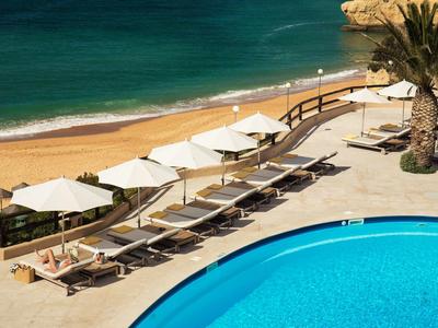 Espace piscine avec transats et parasols à côté de la plage de sable et de la mer
