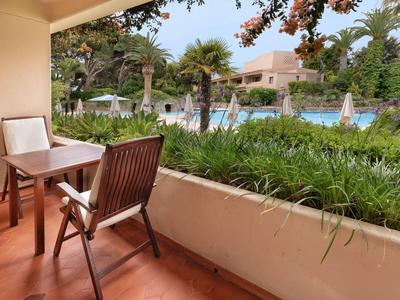 Balcon avec table et chaise donnant sur une piscine et des palmiers dans un jardin d'hôtel