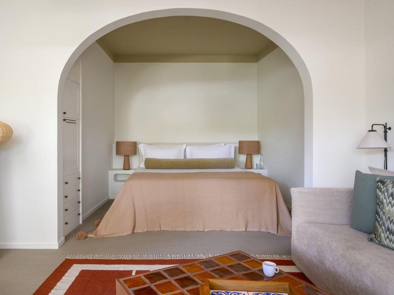 Chambre avec lit double, murs beiges, canapé et tapis décoratif.