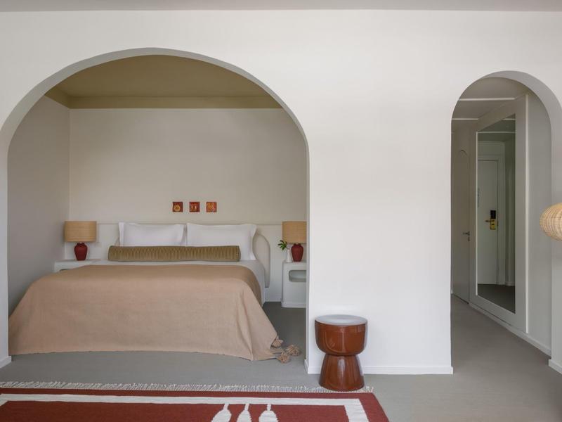 Chambre avec lit double, dessus de lit marron, tables de chevet et murs voûtés dans une chambre d'hôtel.