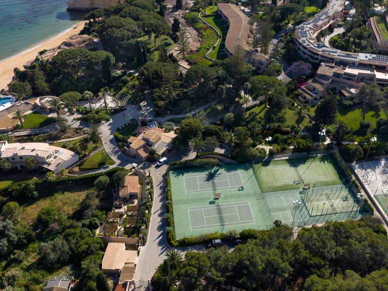 Vue aérienne d'une station de vacances avec courts de tennis, plage et zones boisées.