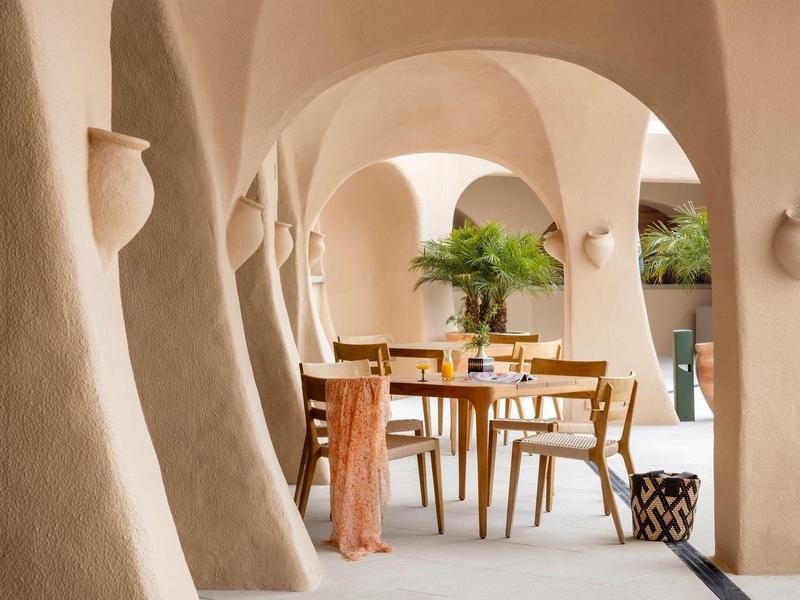 Espace ouvert avec murs courbes, tables et chaises en bois, décoré de plantes.