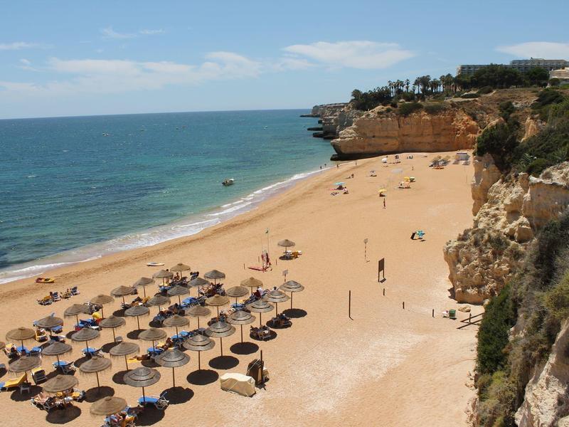 Plage de sable avec parasols et falaises le long de la côte sous un ciel bleu.