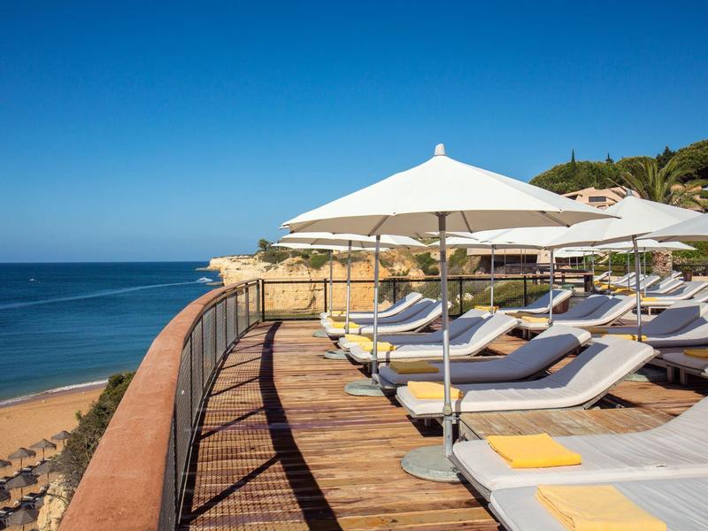 Terrasse ensoleillée avec transats et parasols blancs surplombant la mer