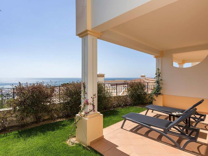 Terrasse couverte avec chaises longues offrant une vue sur la ville et la mer.
