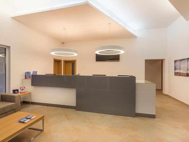 Zone d'accueil moderne avec comptoir gris, table en bois et canapé dans une pièce chaleureusement éclairée.