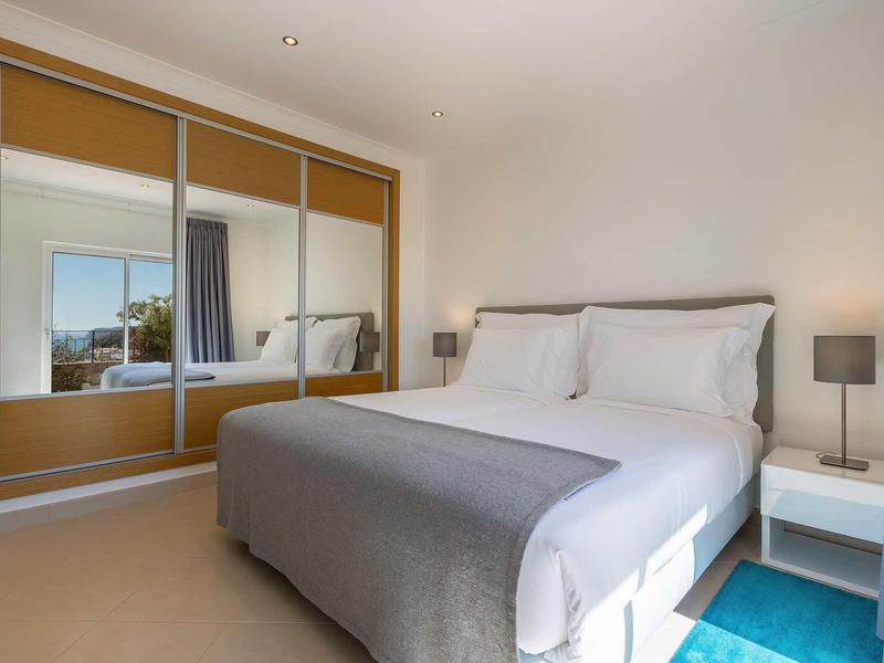 Chambre moderne avec grand lit, couverture grise, table de chevet et armoire avec miroir.