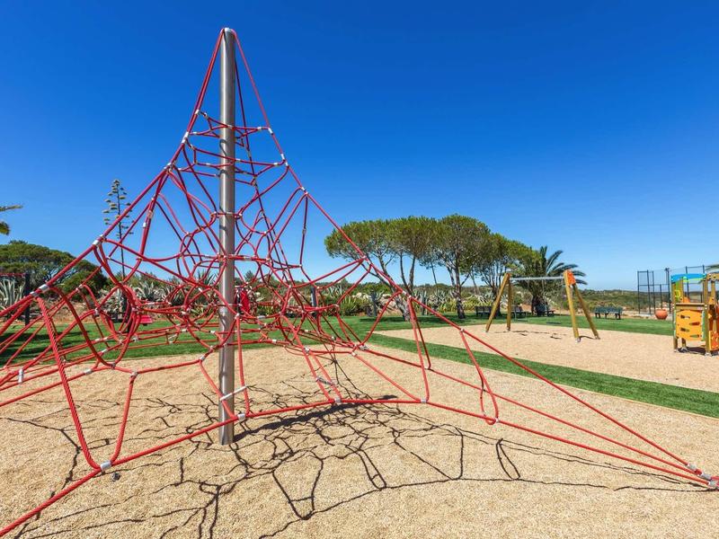 Aire de jeux avec structure d'escalade en corde sur sable sous un ciel bleu clair