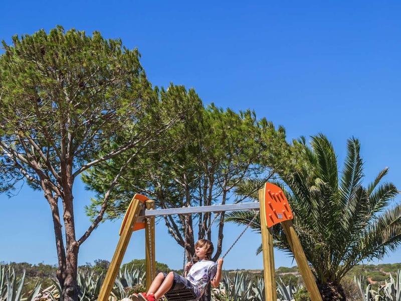 Enfant sur une balançoire en bois sous un ciel bleu dans un parc avec des arbres.
