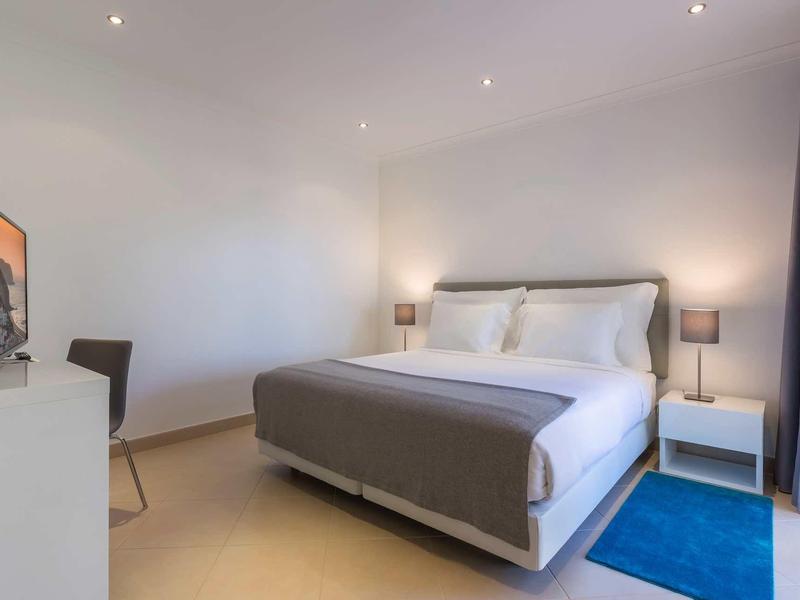 Chambre d'hôtel moderne avec grand lit, lampes de chevet et télévision à écran plat.