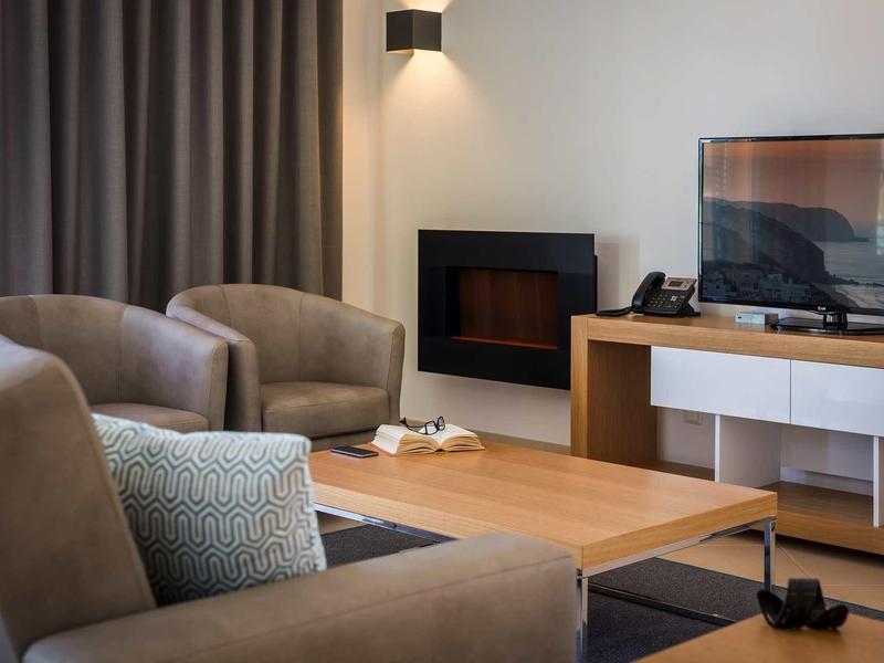 Salon moderne avec fauteuils confortables, télévision et cheminée dans une chambre d'hôtel.