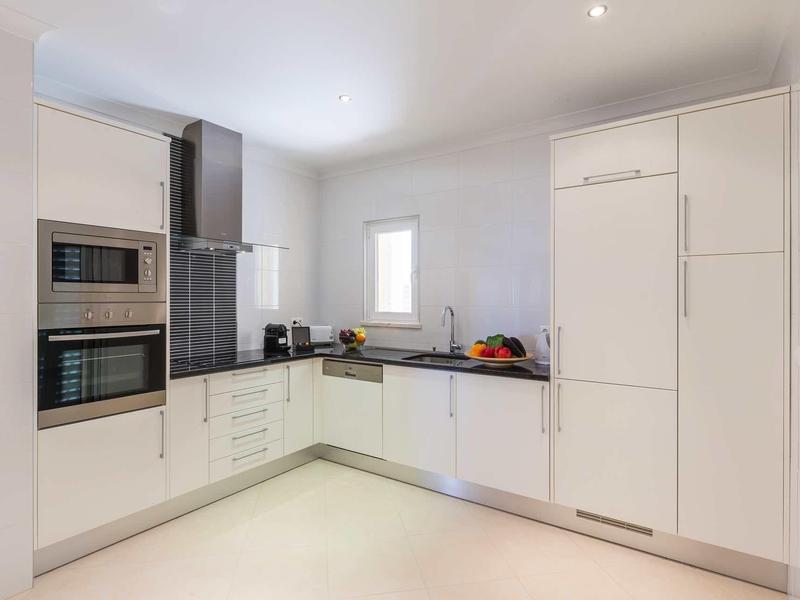 Cuisine moderne lumineuse avec armoires blanches, plans de travail noirs et appareils intégrés.