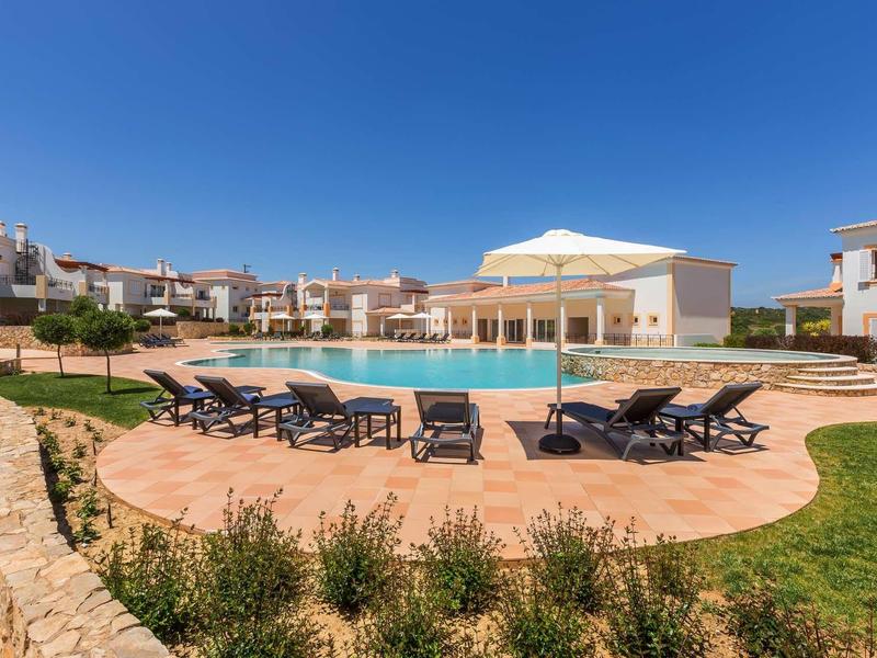 Grande piscine avec chaises longues et bâtiments modernes sous un ciel bleu clair.
