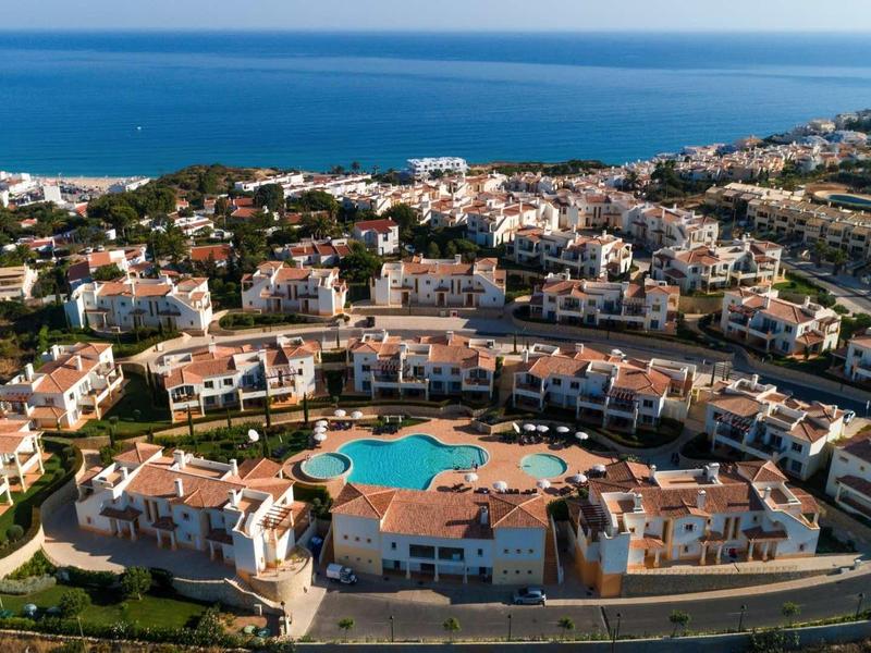 Vue aérienne d'une station balnéaire avec piscine, bâtiments blanchis à la chaux, et mer en arrière-plan