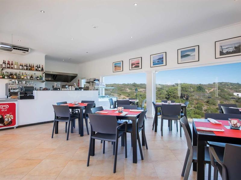 Restaurant moderne avec chaises noires, nappes rouges et grandes fenêtres offrant une vue.