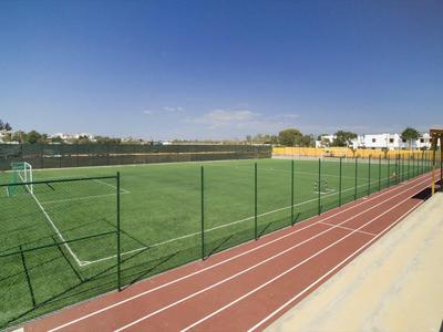 Ein Fußballfeld mit grünem Kunstrasen, umgeben von einem Laufband und einem Zaun im Freien.