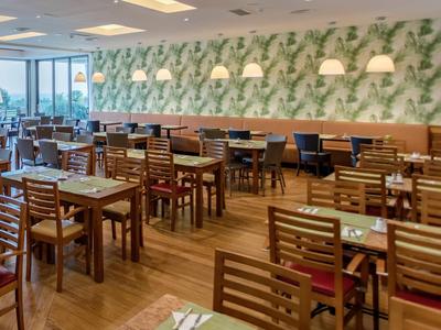 Licht restaurant met houten tafels, stoelen en botanische wanddecoratie.